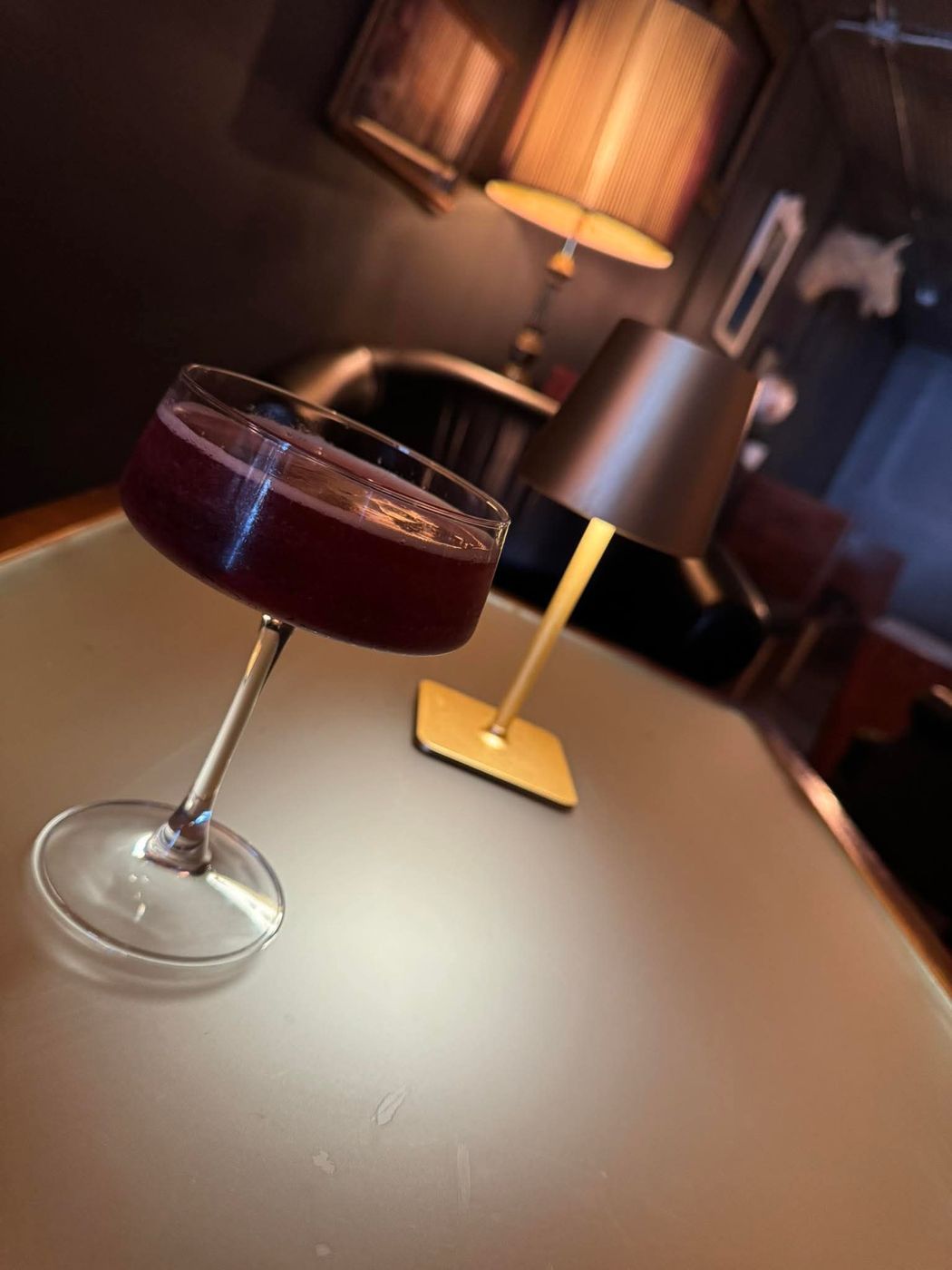 A deep red cocktail in a coupe glass beside a gold table lamp