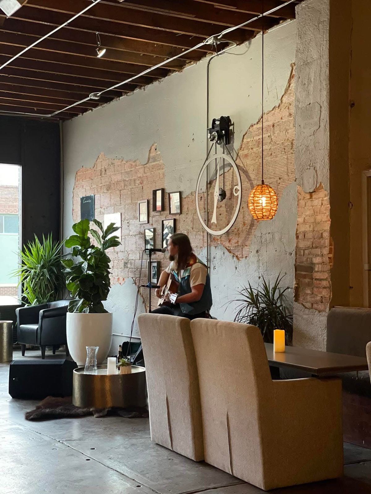 A singer-songwriter playing acoustic guitar against the Reno Tavern’s exposed brick wall